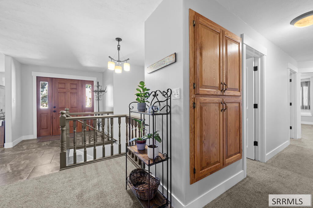 Entry foyer with a wood front door, matching tall cabinets, tiled flooring, and a stair railing.