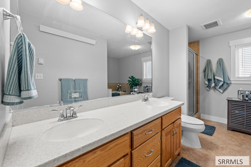 Bathroom with a long double vanity, wood cabinetry, and a large mirror.