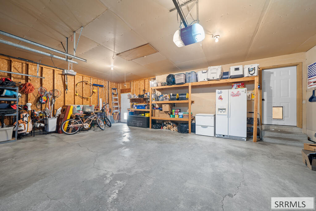 Spacious garage with concrete floor, storage shelves, bicycles, and a refrigerator and freezer.
