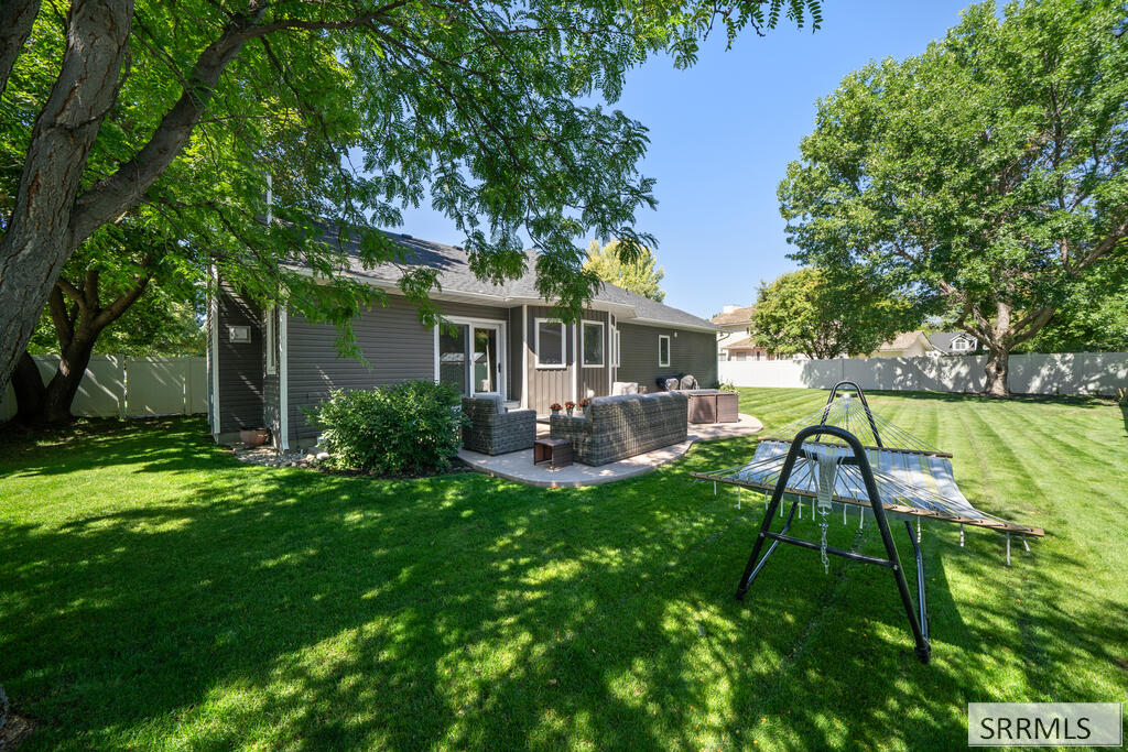 Backyard with a shaded patio, outdoor seating, and a hammock beside a broad lawn.