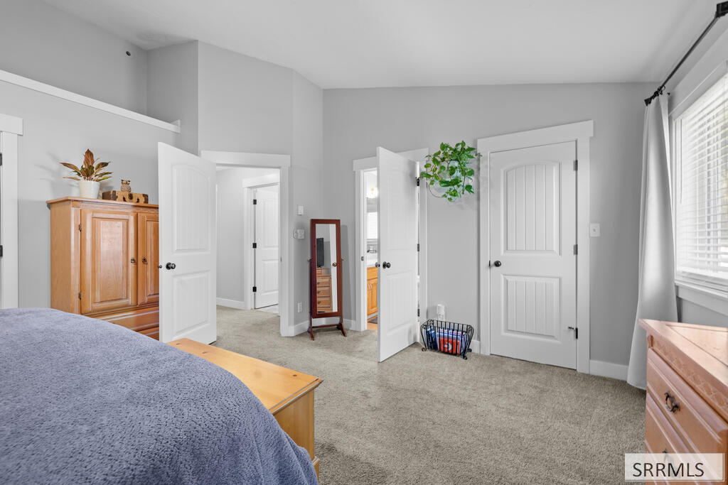 Bedroom with a blue-covered bed, wooden dressers, and several white doors.