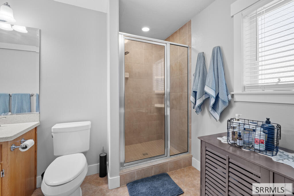 Bathroom with a glass-enclosed tile shower, blue towels, and a shuttered window.