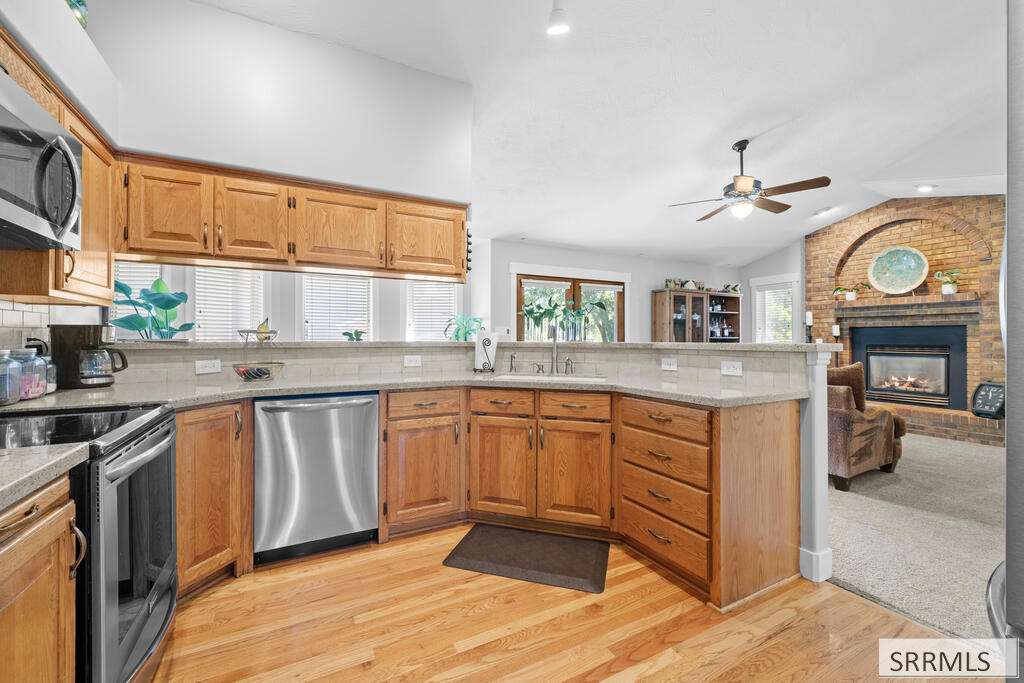 Kitchen with wood cabinets and stainless steel appliances, opening to a living room with a brick fireplace.