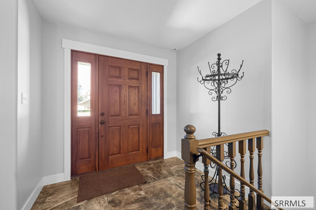 Entry foyer with a paneled wood front door, tile flooring, and a wooden stair railing.