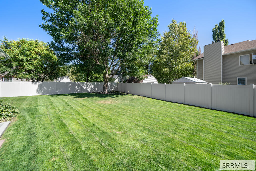 Backyard with a broad green lawn, mature trees, and a white privacy fence.
