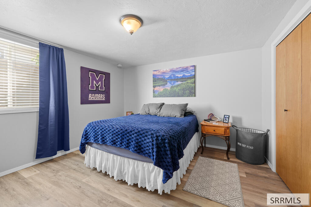 Bedroom with a blue-covered bed, purple Raiders banner, and wooden nightstand.