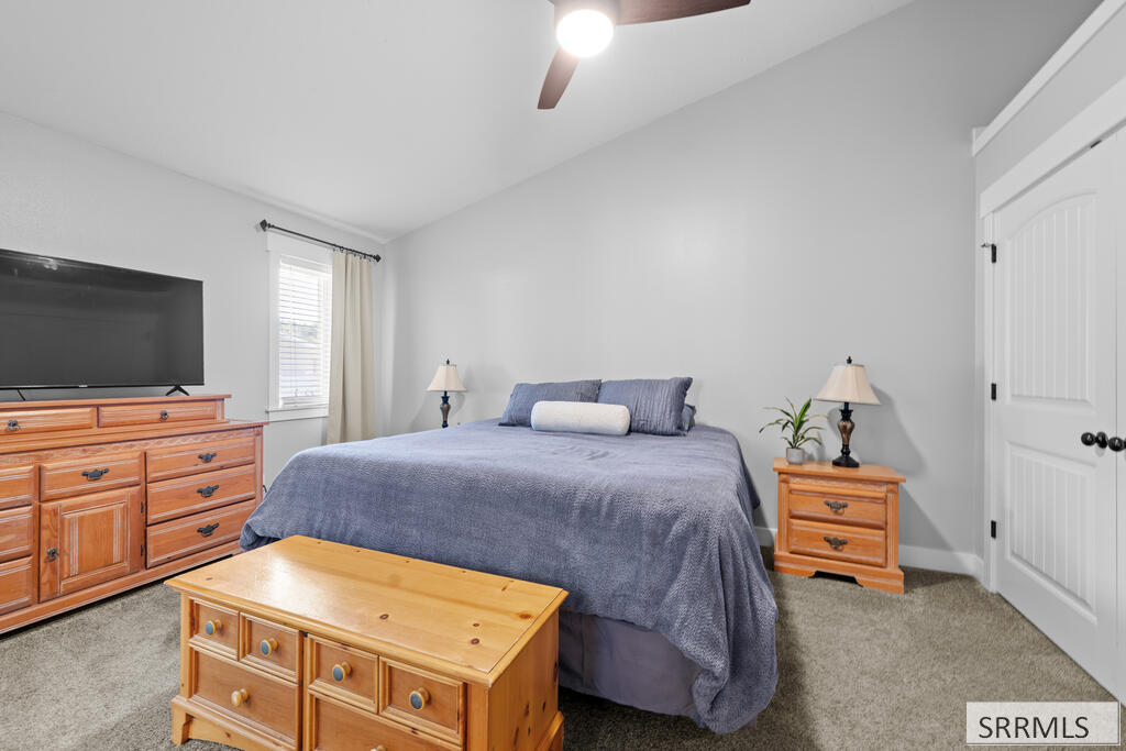 Furnished bedroom with a blue-gray bedspread, matching wooden dressers, and a television.