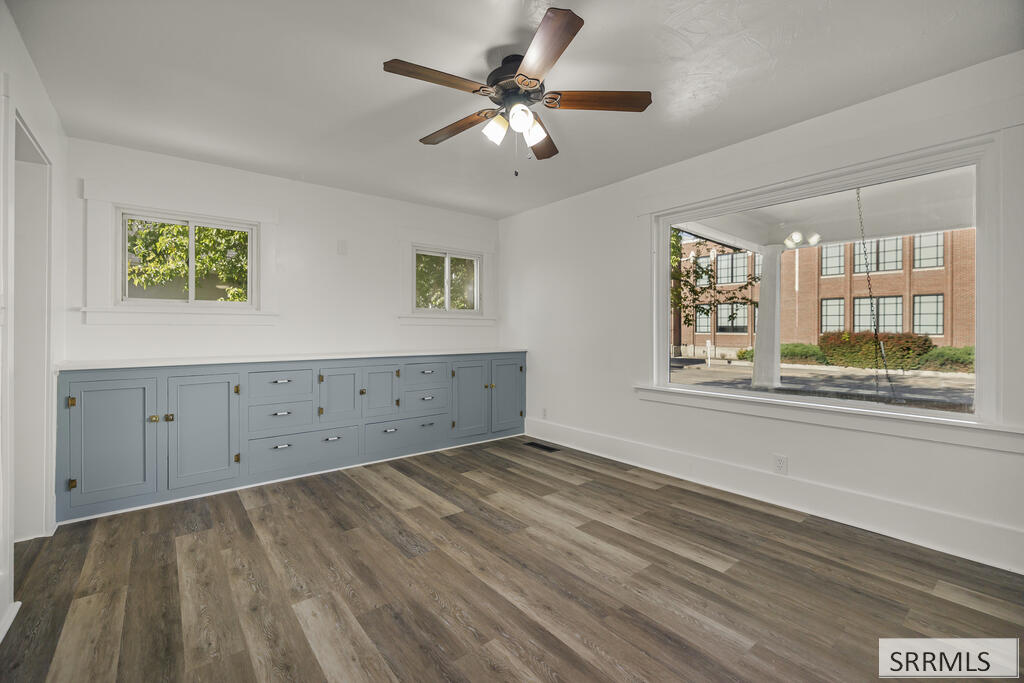 Empty room with blue-gray built-in cabinets, wood-look flooring, and large windows.