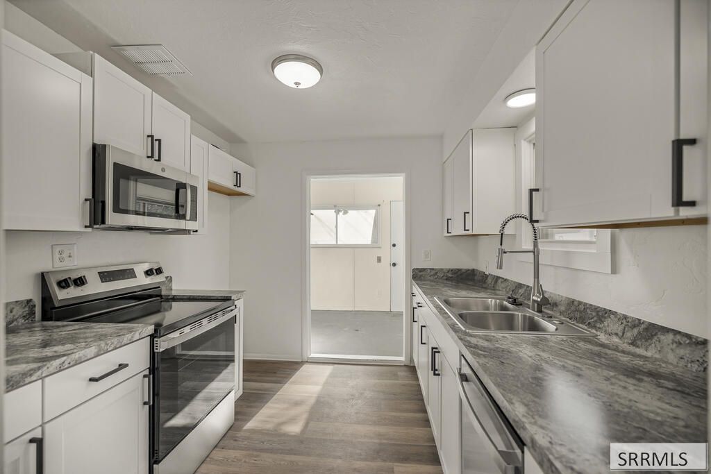 Kitchen with white cabinets, gray countertops, stainless steel appliances, and a doorway to a sunlit room.