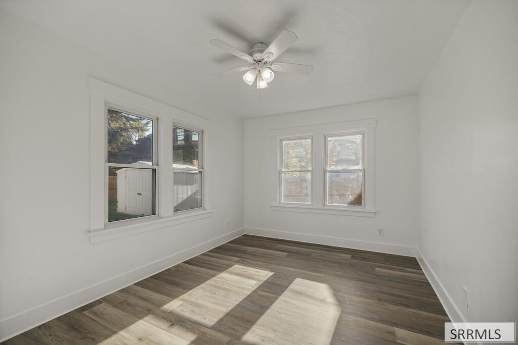 Empty room with dark wood-look flooring, three windows, and a white ceiling fan.