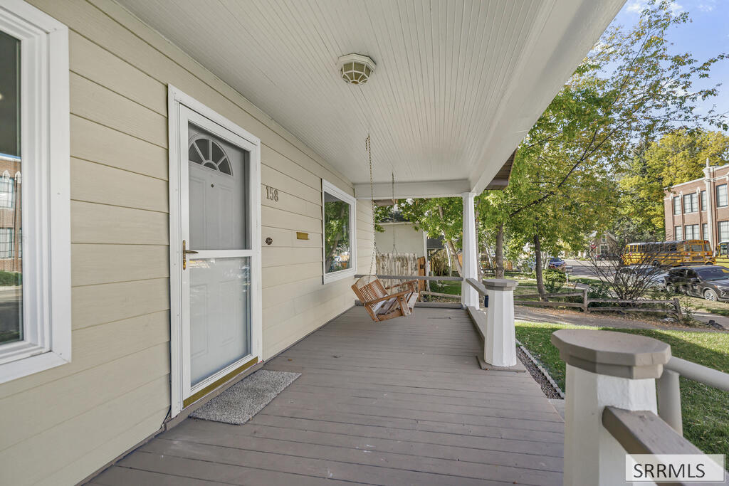 Covered front porch with a gray deck, white railings, and a wooden bench.