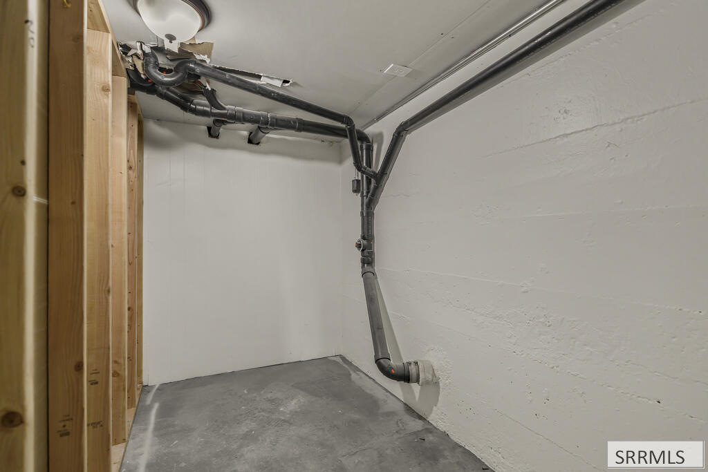 Unfinished utility space with exposed framing, overhead pipes, and a concrete floor.
