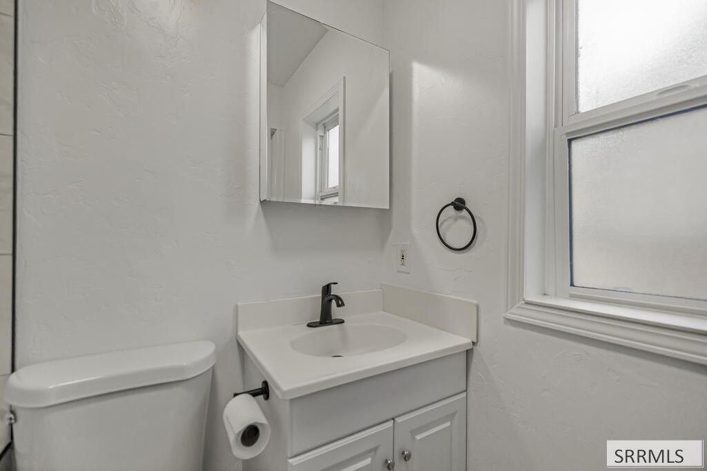 White bathroom vanity with dark faucet beside a toilet and frosted window.