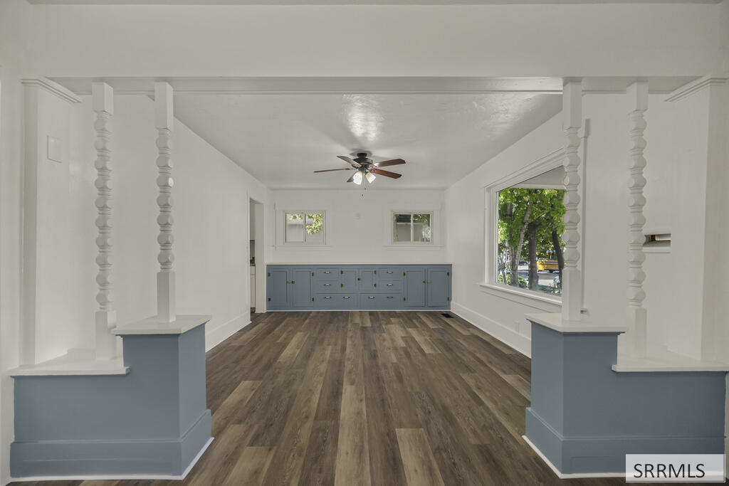 Vacant room with blue-gray built-in cabinets, decorative columns, and dark wood-look flooring.