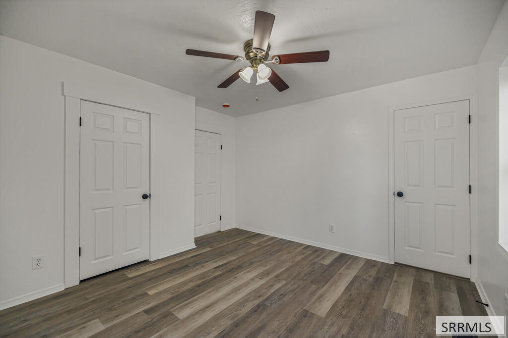 Empty room with plank flooring, a ceiling fan, and three paneled doors.