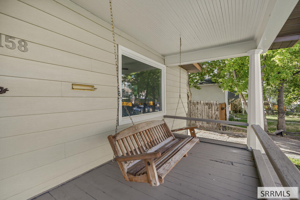 Covered front porch with a chain-hung wooden swing and leafy trees beyond the railing.