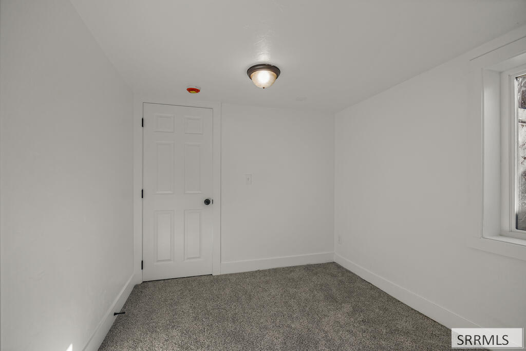 Vacant bedroom with gray carpet, white walls, and a window.