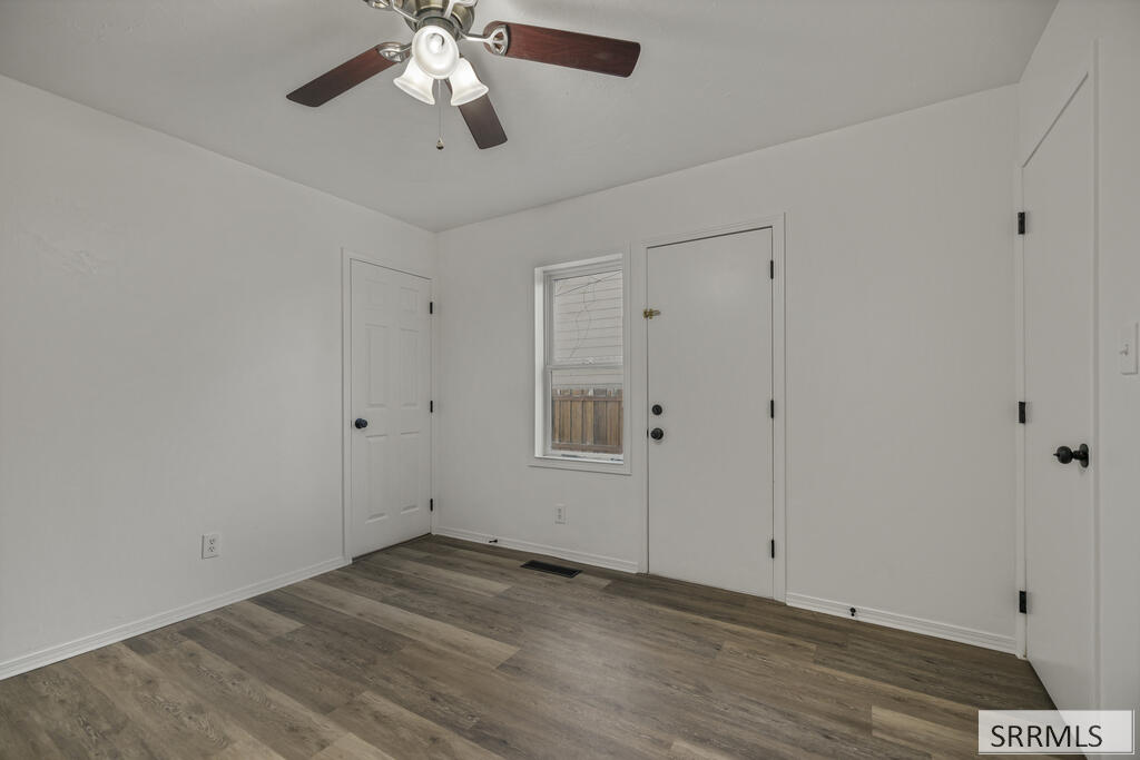 Empty room with gray-brown plank flooring, a ceiling fan, and a window between two doors.