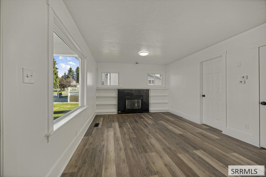 Vacant living room with gray plank flooring, a large window, and a fireplace between built-in shelves.