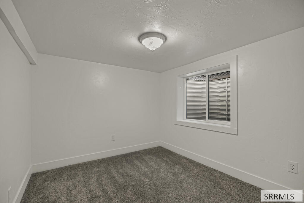 Unfurnished bedroom with gray carpet, white walls, and a shuttered window.