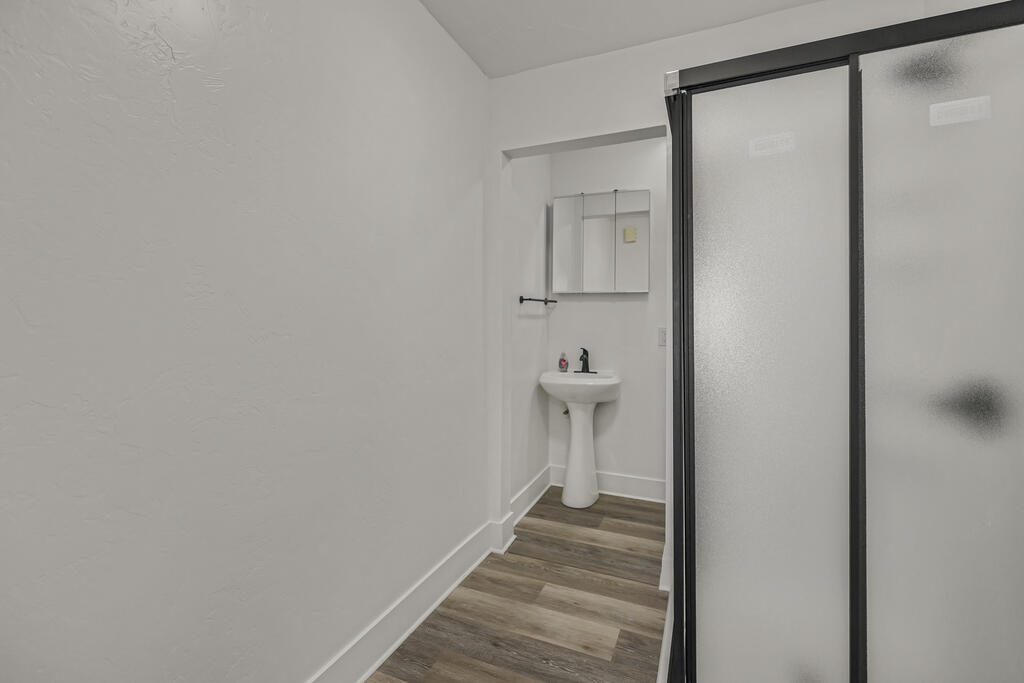 Bathroom with a frosted-glass shower enclosure, pedestal sink, and wood-look flooring.