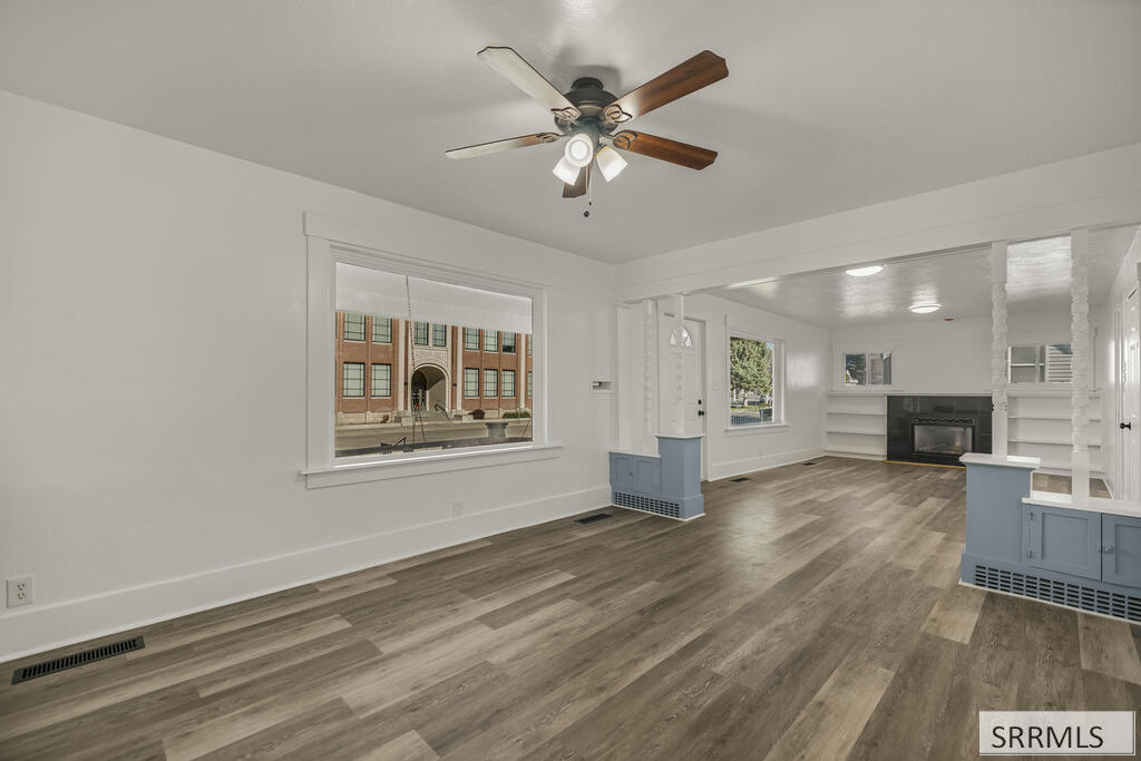 Vacant living room with wide-plank flooring, built-in shelves, and a fireplace.