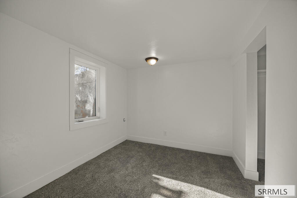 Empty bedroom with gray carpet, a single window, and an open closet area.