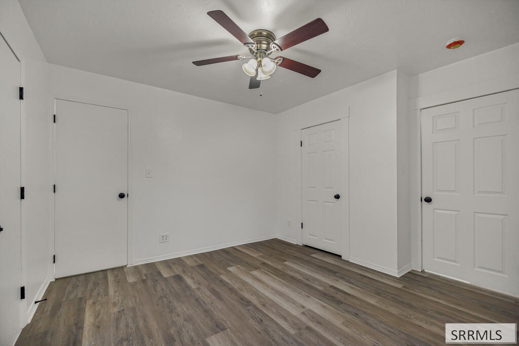 Empty room with gray-brown plank flooring, a ceiling fan, and several white doors.