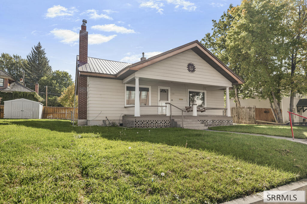 Single-story home with a covered porch, metal roof, brick chimney, and green lawn.