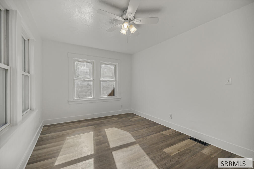 Vacant bedroom with wood-look flooring, two windows, and a ceiling fan with lights.