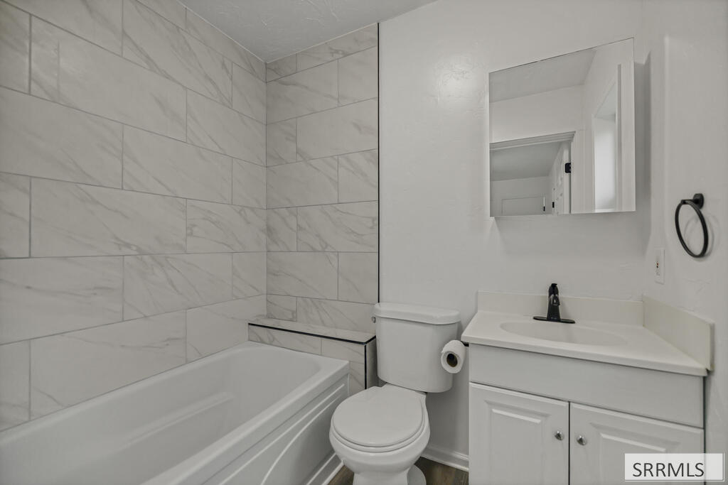 Bathroom with marble-look tile, white bathtub, toilet, and vanity with a black faucet.