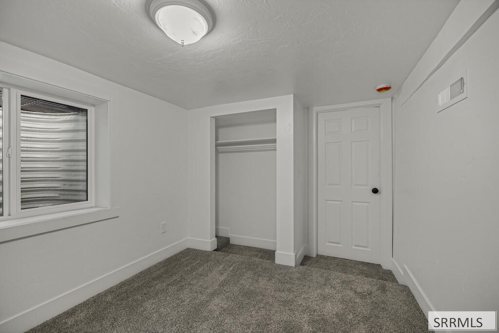 Empty carpeted bedroom with an open closet, striped window shade, and white paneled door.