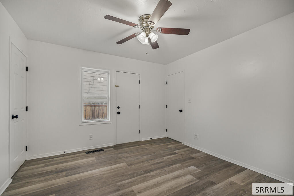 Empty room with gray wood-look flooring, a ceiling fan, and a window with blinds.