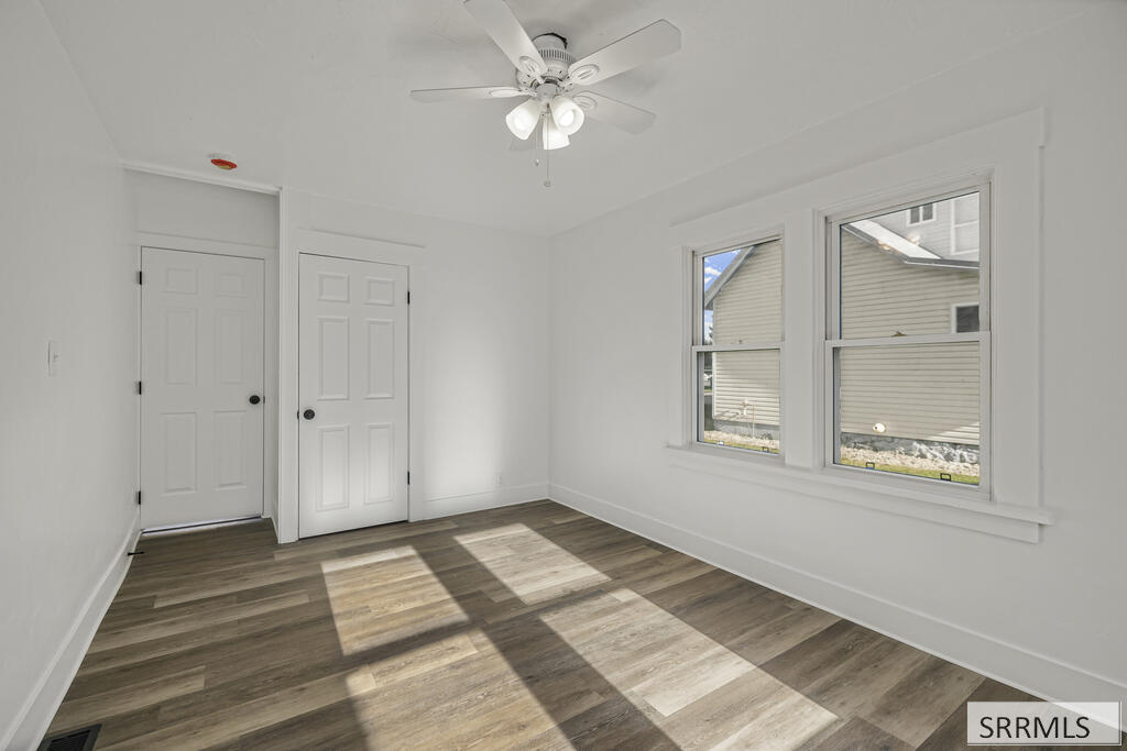 Empty room with wood-look flooring, a ceiling fan, two windows, and two white doors.