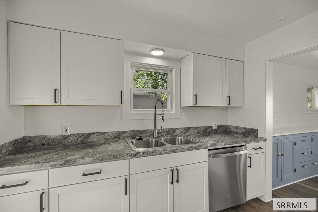 Kitchen with white cabinets, gray stone counters, a double sink, and stainless steel dishwasher.