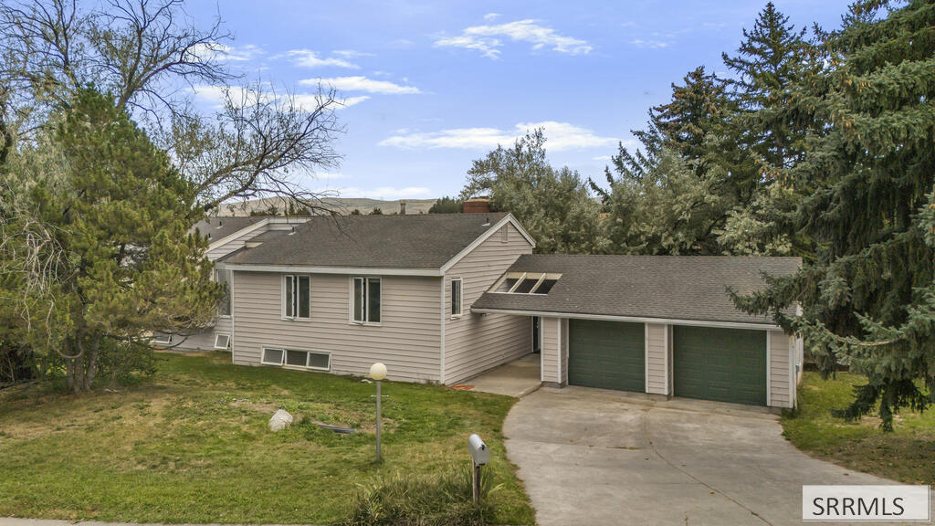 Beige-sided home with a two-car garage and concrete driveway, surrounded by mature trees.