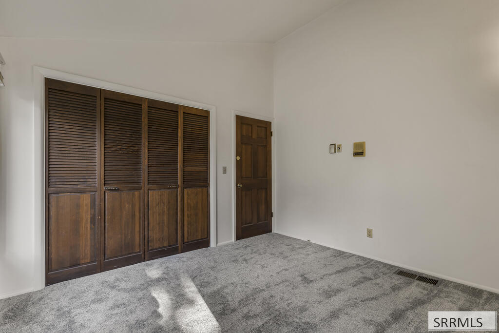 Empty carpeted room with dark wood louvered closet doors and sunlight across the floor.