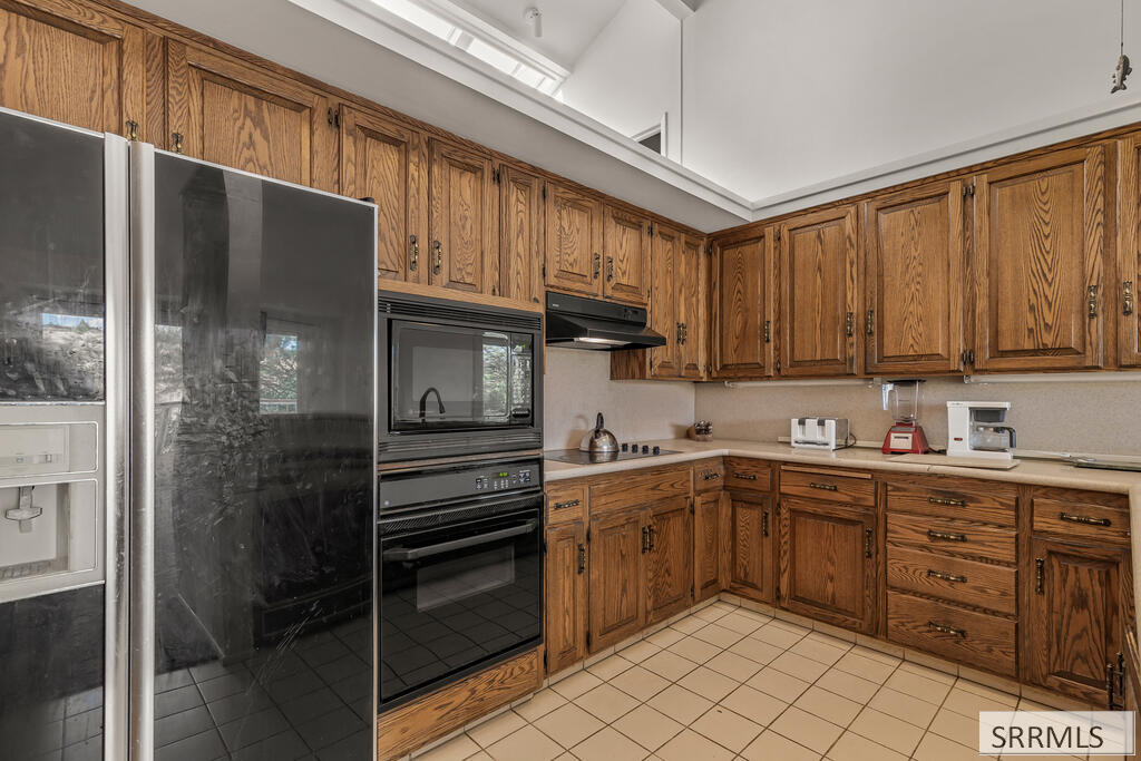 Kitchen with honey-toned wood cabinetry, stainless steel refrigerator, and built-in oven and microwave.