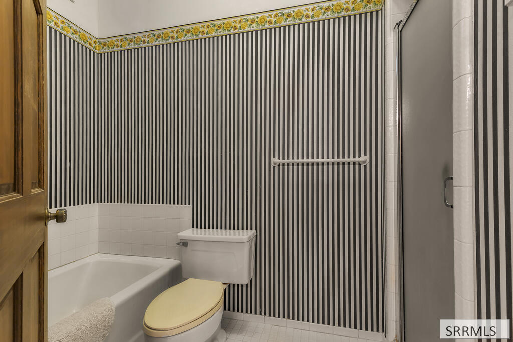 Bathroom with striped walls, a white bathtub, toilet, and separate shower.