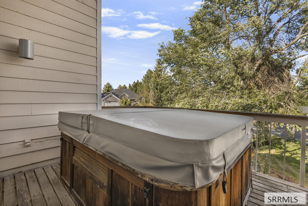 Covered hot tub on a wooden deck beside the house, overlooking leafy trees.