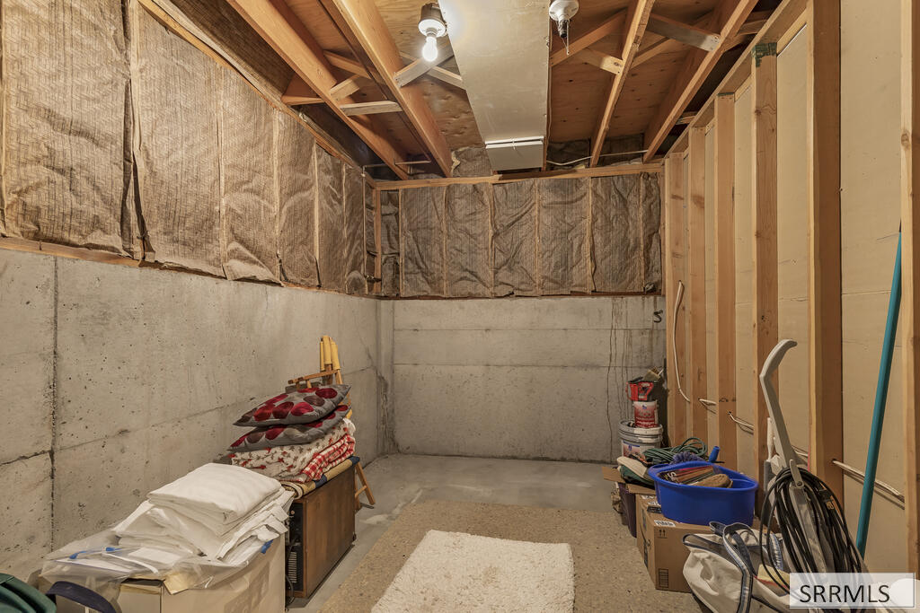 Unfinished basement with exposed ceiling framing and insulation, concrete walls, and stored household items.