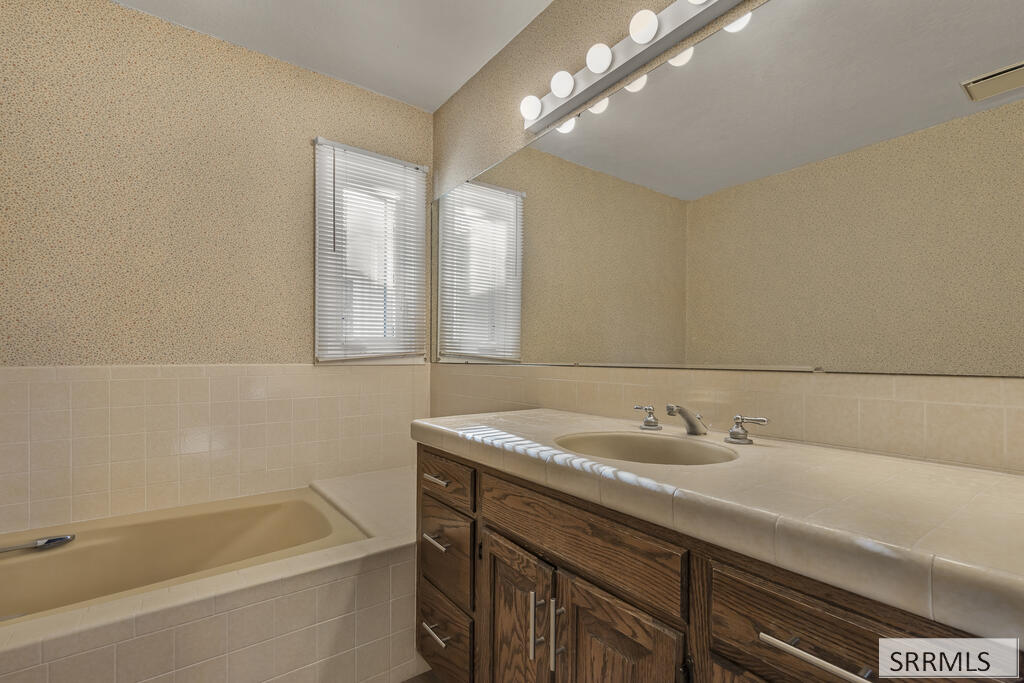 Bathroom with a beige bathtub and wood vanity beneath a large mirror.