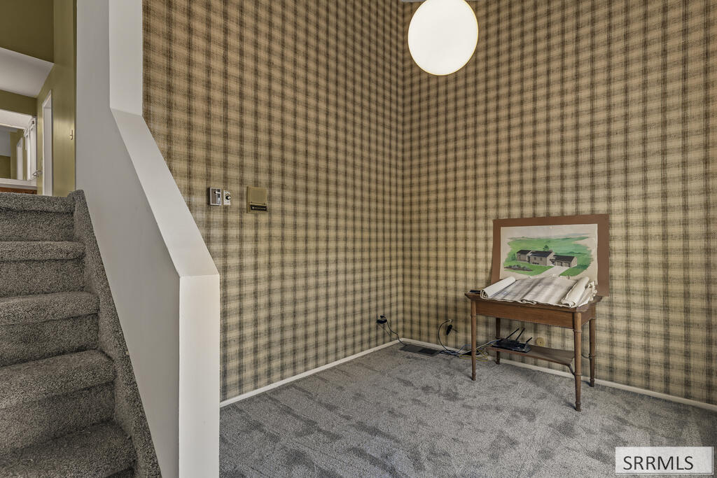 Carpeted stair landing with plaid wallpaper and a wooden table holding rolled plans.