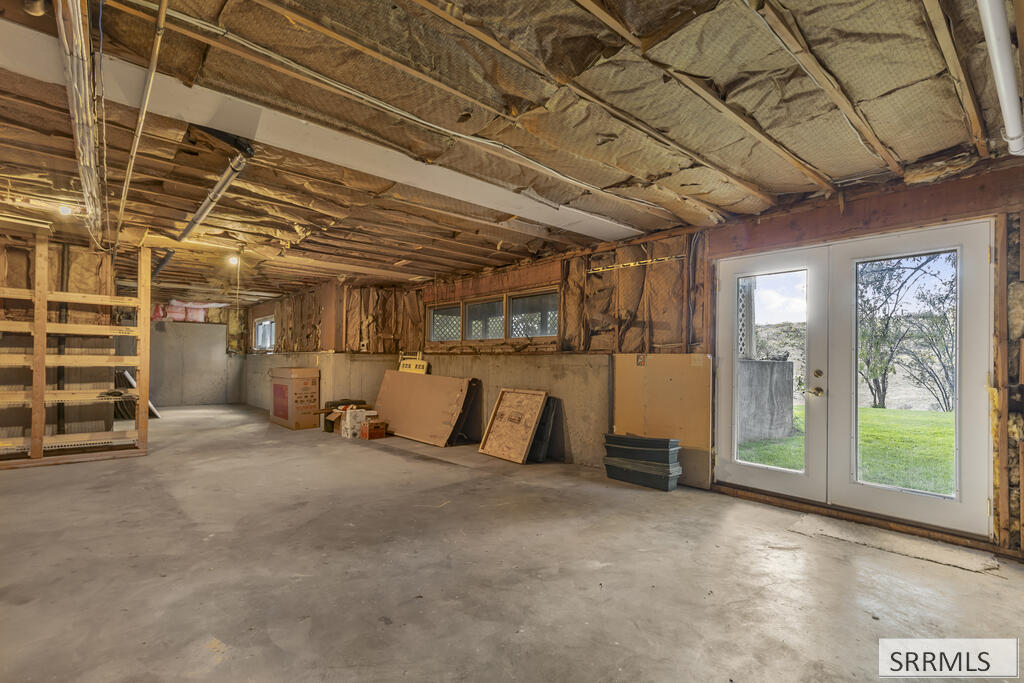 Unfinished basement with exposed insulation and framing, concrete floor, and double doors opening to the yard.