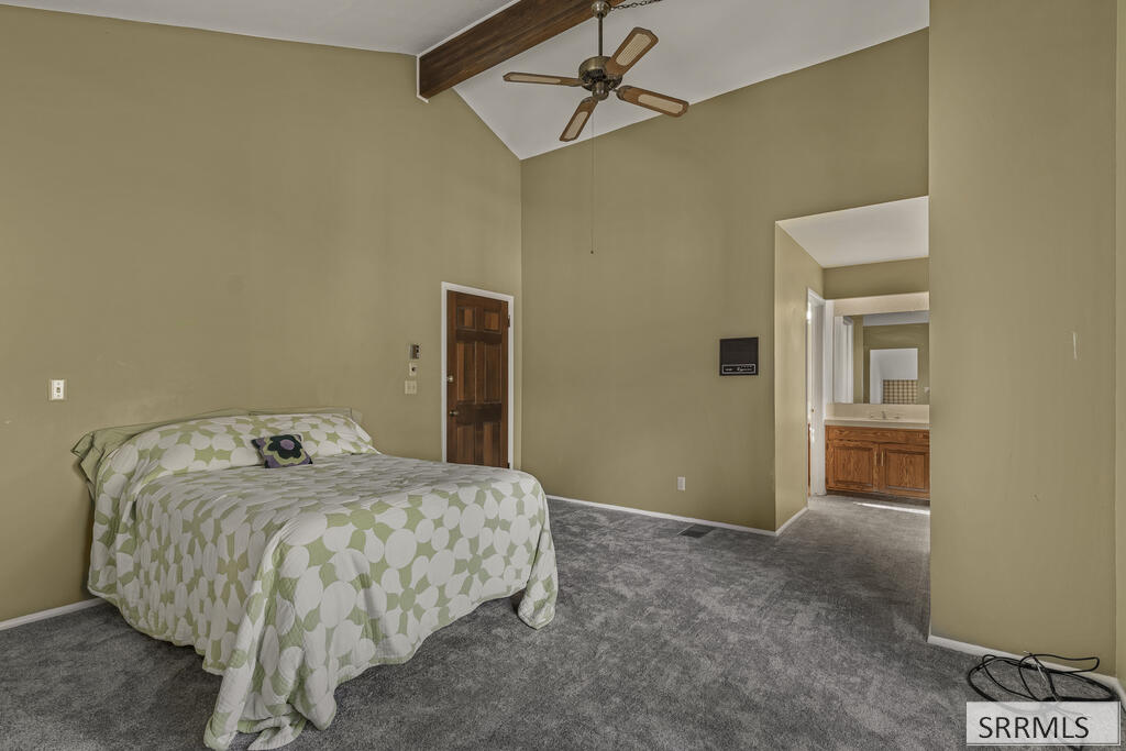 Bedroom with a patterned bedspread, vaulted ceiling, and doorway to a bathroom.