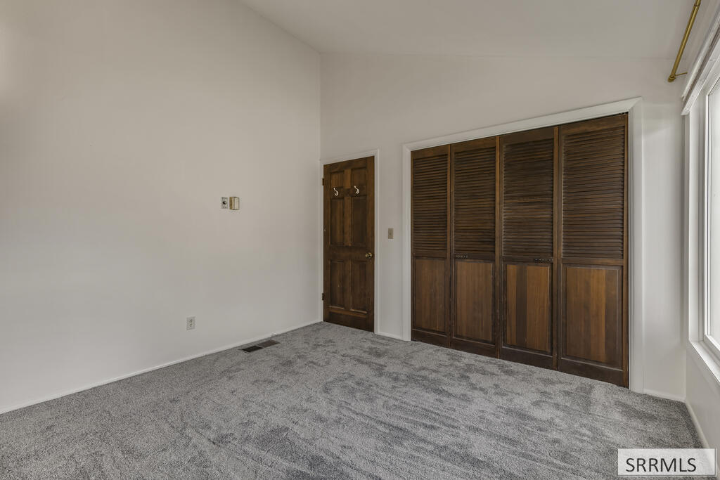 Vacant carpeted room with dark wood louvered closet doors and a large window.