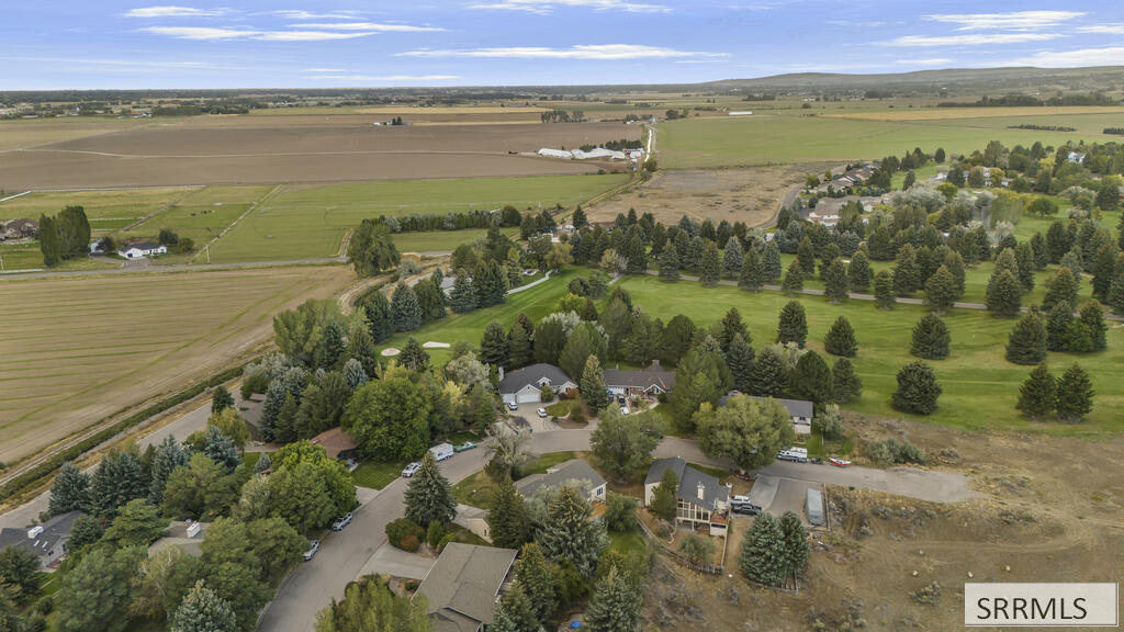 Aerial view of homes among mature trees beside an expansive landscaped green space and open fields.