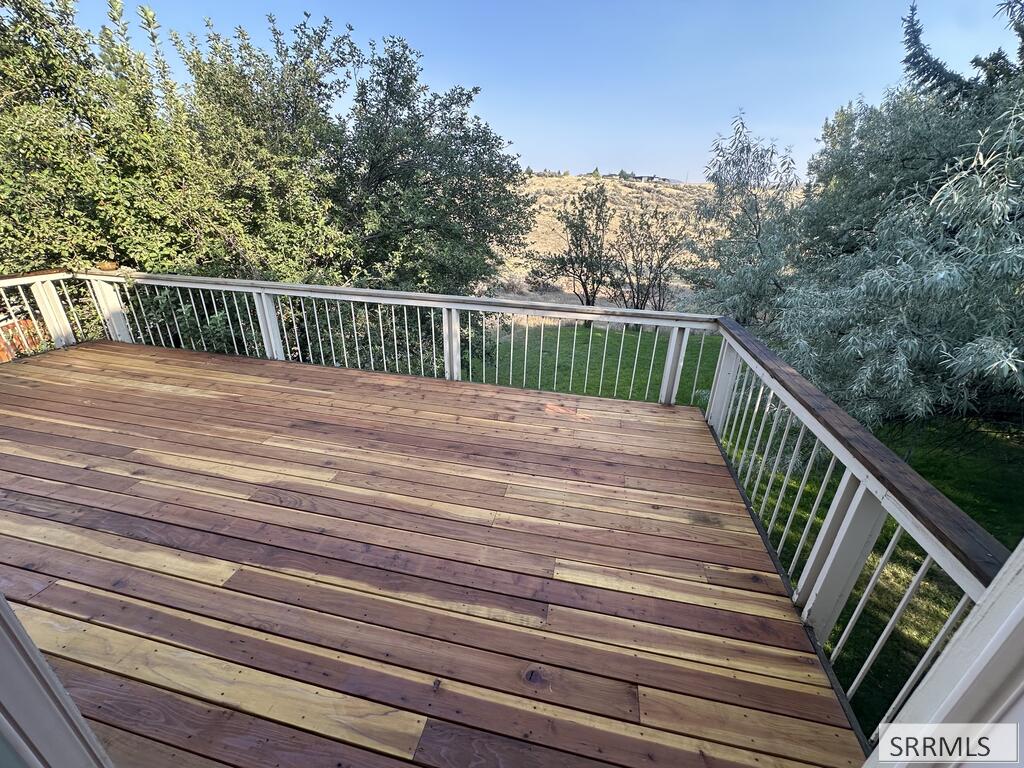 Wooden deck with white railings overlooking a tree-lined backyard and distant hillside.