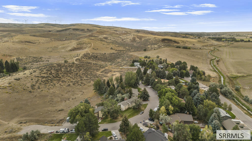 Aerial view of a tree-lined neighborhood beside open rolling hills and distant wind turbines.