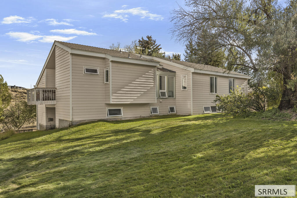Beige-sided house on a grassy slope, with a small deck and mature trees.